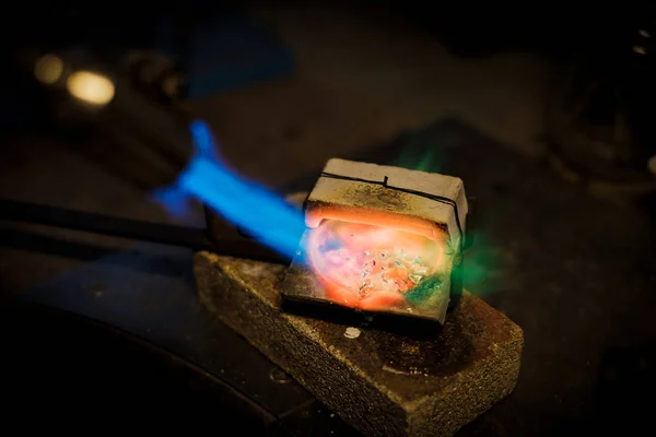 Jeweler melts with a flame silver or gold on old workbench in jewelers workshop