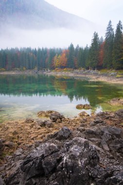 Görüntülemek göl üzerinde Laghi di Fusine plaj ve dağ silsilesi Mangart Tarvisio İtalya yakınındaki bazı taşlara bir sisli sabahı
