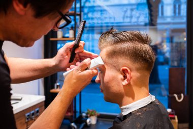 Berber, berber dükkanında ustura olan genç bir adamın saçını kesiyor.