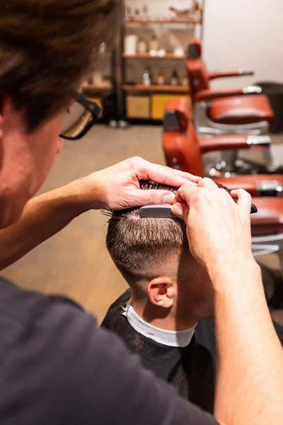 Barber shaves the parting of a young man\'s hair with a razor blade in his barbershop
