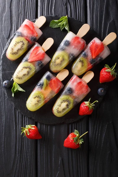 popsicles ice on a stick of strawberry, kiwi and blueberries with mint closeup on the table. Vertical top view from abov