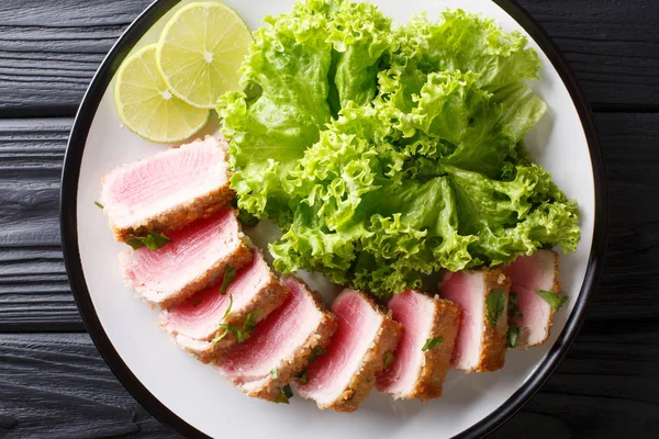 stock image Delicious steak ahi tuna  in bread crumbs panko with lettuce and lime closeup on a plate on a black table. horizontal top view from abov