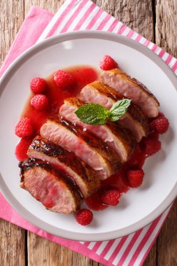 Lezzetli yiyecek kızarmış ördek göğsü taze ahududu ile dilimlenmiş sos ve nane closeup masada bir tabakta. Abov gelen dikey üstten görünüm