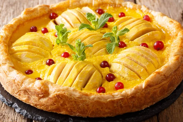 open apple pie with cranberries and custard is decorated with mint close-up on the table. horizonta