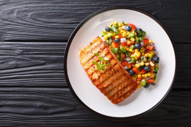 Taze biber, Mısır, yaban mersini ve soğan salata yakın çekim bir tabloda bir tabakta ile ızgara somon fileto pişmiş. abov üzerinden yatay üstten görünüm