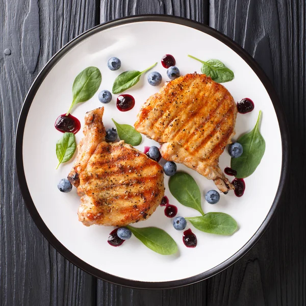 Barbekü gıda: ızgara domuz eti biftek kaburga ile ahşap bir masa üzerinde bir plaka üzerinde taze yaban mersini sosu ve ıspanak closeup ile. abov üzerinden üstten görünüm