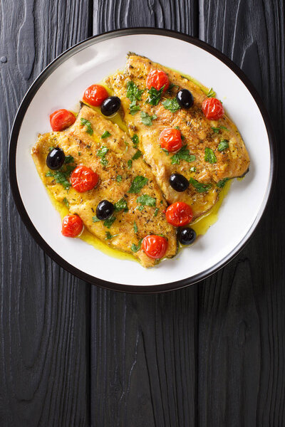 Fried trout fillets with garlic butter sauce, tomatoes and olives closeup on a plate. Vertical top view from abov