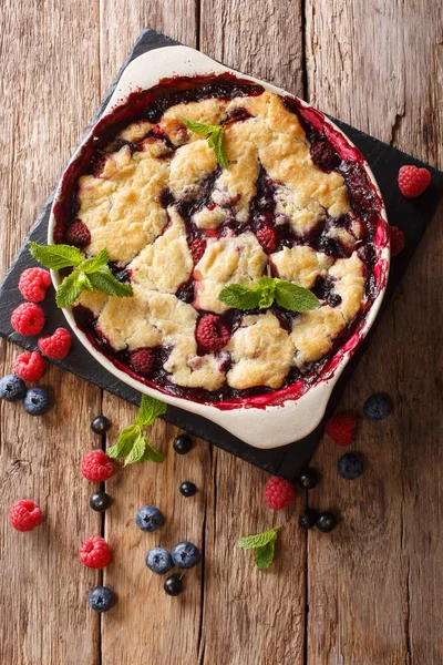 Summer berry cake with raspberry berries, currants and blueberries close-up in a baking dish on a table. vertical top view from abov