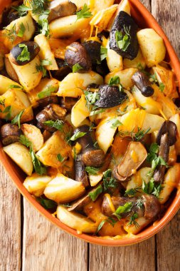 Pişmiş patates dilimleri ile orman mantar, kaşar peynir ve otlar yakın bir pişirme içinde bir masada çanağı. Abov gelen dikey üstten görünüm