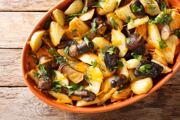 Baked potato wedges with forest mushrooms, cheddar cheese and herbs close-up in a baking dish on a table. horizontal top view from abov