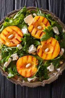 Lezzetli meze beyaz peynir, roka, fıstık ve otlar yakın çekim bir plaka üzerinde bir tablo ile ızgara Taze şeftali salatası. Abov gelen dikey üstten görünüm