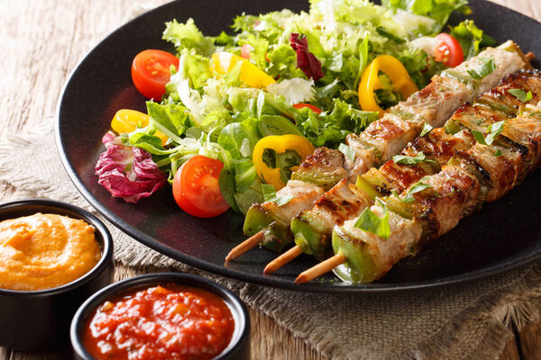 Delicious food: pork with vegetables on skewers with fresh salad on a plate and ketchup and mustard close-up on a table. horizonta