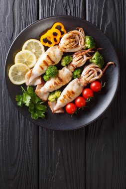 Izgara kalamar tentacles ile domates, brokoli, bir tabloda bir tabakta limon ve biber closeup ile. abov gelen dikey üstten görünüm