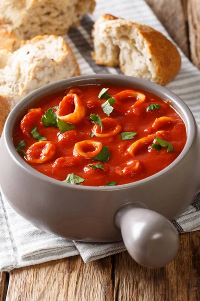 Hot stewed: calamari in tomato with spices and herbs close-up in a pot, with bread. vertica