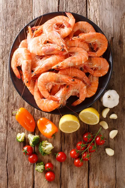Boiled shrimp with broccoli, lemon, garlic, tomatoes and pepper closeup on a wooden table. vertical top view from abov