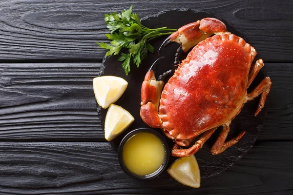 Delicious traditional boiled whole brown crab with sauce, lemon and parsley on a slate board close-up on a black table. Horizontal top view from abov