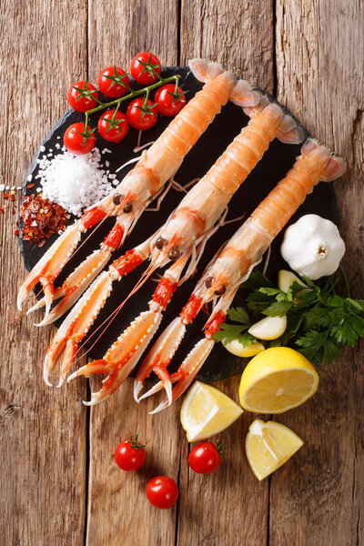 Luxury fresh raw langoustine, scampi with ingredients close-up on a wooden table. Vertical top view from abov