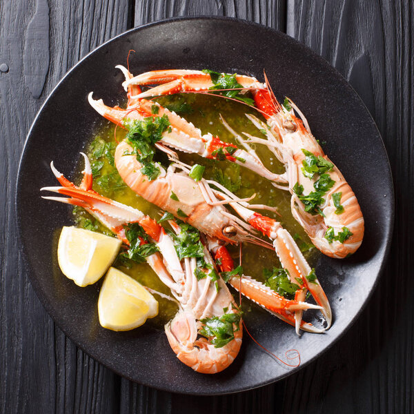 Delicious boiled scampi or langoustine or Norway lobster close-up on a plate with sauce and lemon on a table. top view from abov