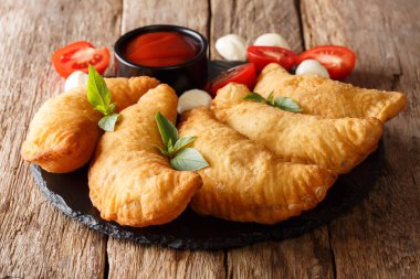 Domates, otlar ve mozzarella yakın çekim bir dolgulu sıcak kızarmış panzerotti bir kara tahta üzerinde servis edilir. Horizonta