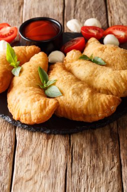 Ahşap bir masa üzerine domates sosu ve mozzarella closeup ile lezzetli sıcak kızarmış panzerotti. Vertica