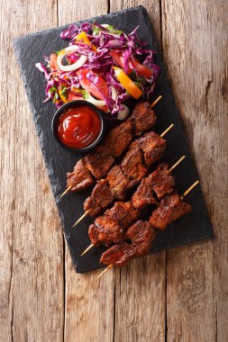 Recipe of a spicy African suya kebab on skewers with fresh vegetable salad and ketchup close-up on a table. vertical top view from abov clipart