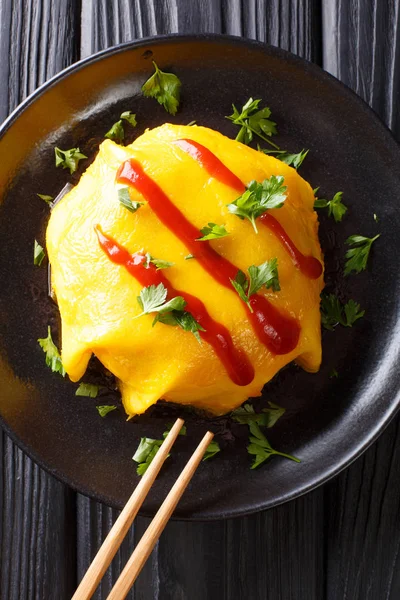 ahşap bir masa üzerinde siyah bir plaka üzerinde pirinç, tavuk, sebze ve domates soslu Japon omlet tarifi. Abov gelen dikey üstten görünüm