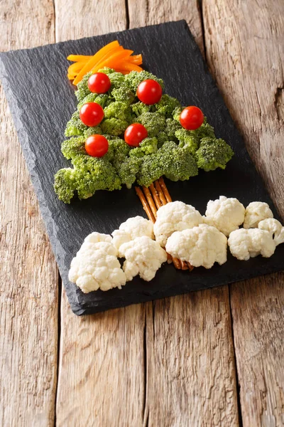 Christmas tree made of fresh vegetables broccoli, cauliflower, tomatoes, peppers close-up on the table. Vegetarian menu. vertica