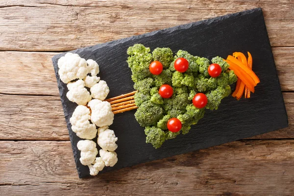 Beautiful food: Christmas tree of broccoli, cauliflower, tomatoes, pepper closeup on a table. Horizontal top view from abov