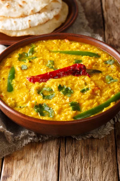 Dal Tadka yellow lentil Indian soup with flat bread on a wooden background close-up. Vertica