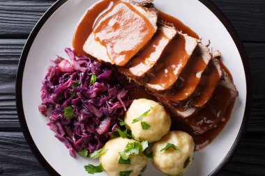 German roast pot Sauerbraten served with potato dumplings and red cabbage close-up on a plate. horizontal top view from abov clipart