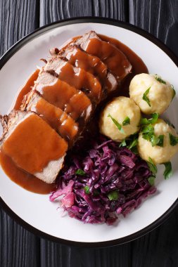 German roast pot Sauerbraten served with potato dumplings and red cabbage close-up on a plate. Vertical top view from abov clipart