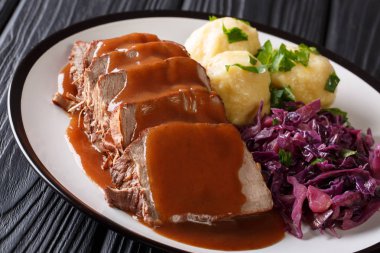Delicious traditional German dinner Sauerbraten - slowly stewed marinated beef with gravy with potato dumplings and red cabbage close-up on a plate. horizonta clipart