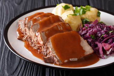 German Sauerbraten is a beef stew with a spicy sauce served with potato dumplings and red cabbage close-up on a plate. Horizonta clipart