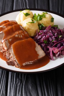 Traditional Sauerbraten dish with potato dumplings and red cabbage close-up on a plate. German cuisine. vertica clipart