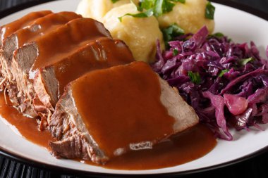 German roast pot Sauerbraten served with potato dumplings and red cabbage close-up on a plate. horizonta clipart