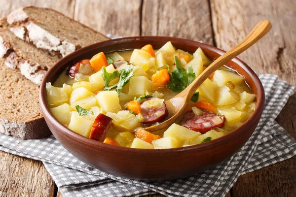 Thick potato soup with sausages and parsley in a bowl with bread close-up on the table. horizonta