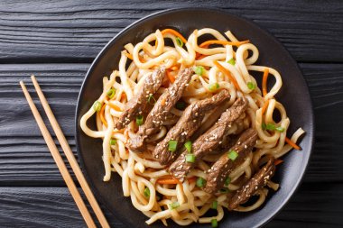 Teriyaki sığır eti udon erişte, havuç ve yeşil soğan yakın masada bir plaka üzerinde çekim. Üstten yatay üstten görünüm. Asya styl