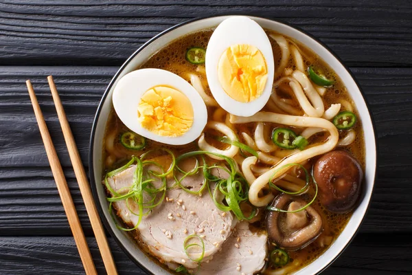 Traditional Japanese udon noodle soup with pork, boiled eggs, mushrooms and green onions closeup in a bowl on the table. horizontal top view from abov