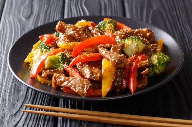 Asya gıda: teriyaki sığır eti ile kırmızı ve sarı biber, siyah bir masaya bir tabak brokoli ve susam tohumu yakın çekim. Horizonta