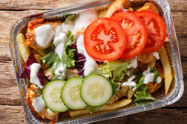 Recipe Dutch fast food kapsalon of french fries, chicken, fresh salad, cheese and sauce close-up in a foil tray on the table. horizontal top view from above