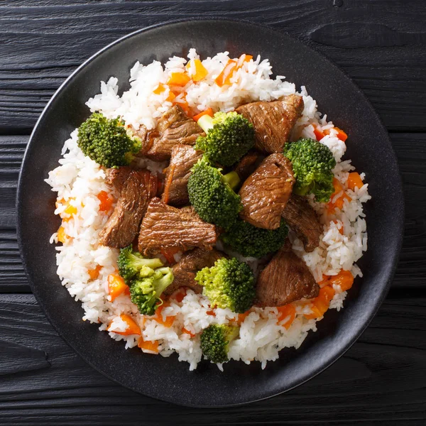 Roasted beef with broccoli with rice and persimmon side dish close-up on a plate on the table. horizontal