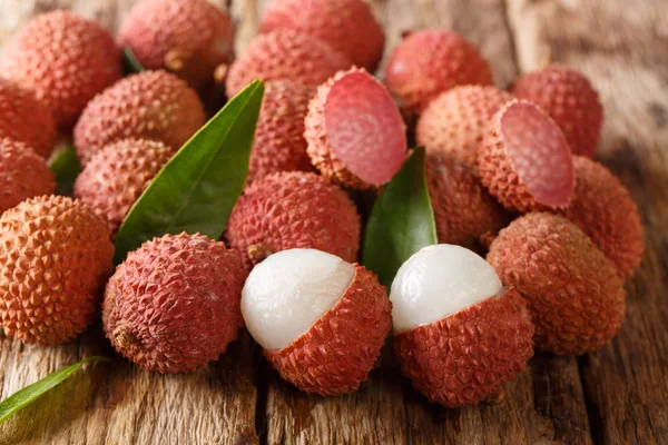 Fresh lychee and peeled showing the red skin and white flesh with green leaf on a wooden background. horizonta