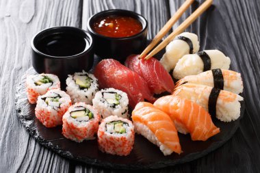 Uramaki ve nigiri suşi siyah plaka closeup ahşap masa üzerinde görev yaptı. Horizonta
