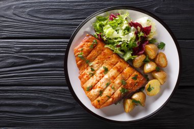 Sağlıklı öğle yemeği kızarmış patates ve taze salata yakın ahşap bir masa üzerinde bir plaka üzerinde çekim ile kılıç balığı fileto ızgara. abov üzerinden yatay üstten görünüm
