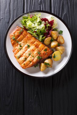Sağlıklı öğle yemeği kızarmış patates ve taze salata yakın ahşap bir masa üzerinde bir plaka üzerinde çekim ile kılıç balığı fileto ızgara. Abov gelen dikey üstten görünüm