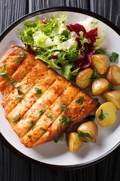 Fried swordfish biftek bebek patates ve ahşap bir masa üzerinde bir tabak taze salata yakın çekim. Abov gelen dikey üstten görünüm