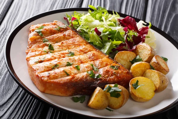 Fried swordfish biftek bebek patates ve ahşap bir masa üzerinde bir tabak taze salata yakın çekim. Horizonta