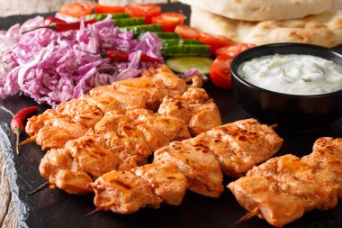 Close-up of chicken skewers with fresh salad, yogurt sauce and pita bread on a slate board. horizonta