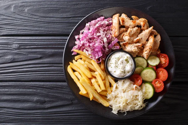 Doner kebab on a plate with french fries, salad and sauce close-up on a wooden table. Horizontal top view from abov