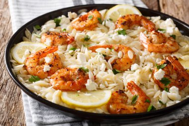 Izgara karides, beyaz peynir, otlar ve limon yakın masada bir plaka üzerinde çekim ile baharatlı orzo makarna. Horizonta